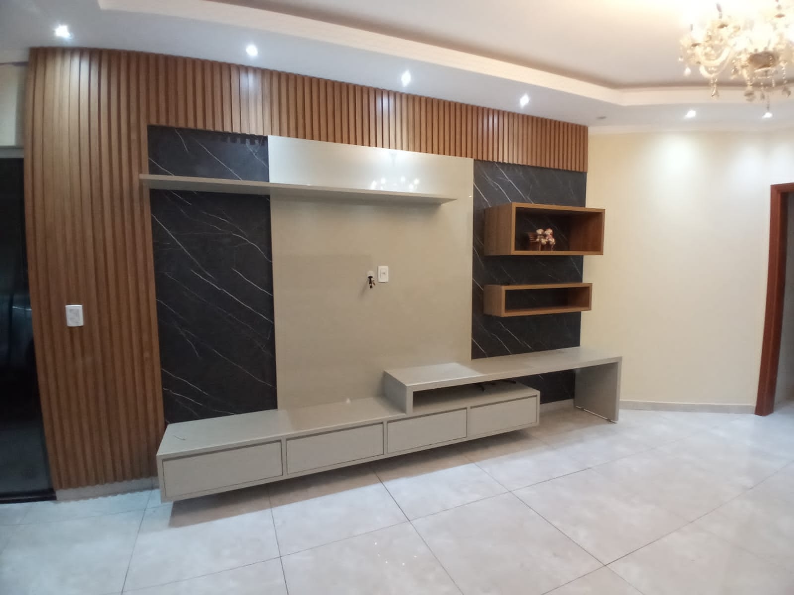 Sala com painel planejado em madeira e detalhes escuros desenvolvida pela Projeto Móveis em Monte Alto SP